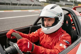 Pilote en combinaison rouge au volant d'une voiture de circuit lors d'un stage de pilotage cadeau